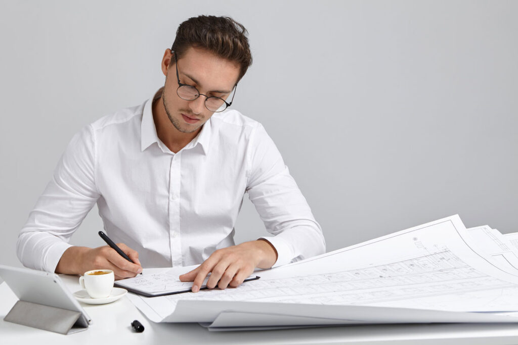 talented-young-european-bearded-chief-engineer-wearing-round-glasses-white-formal-shirt-sitting-his-workplace-construction-document-management