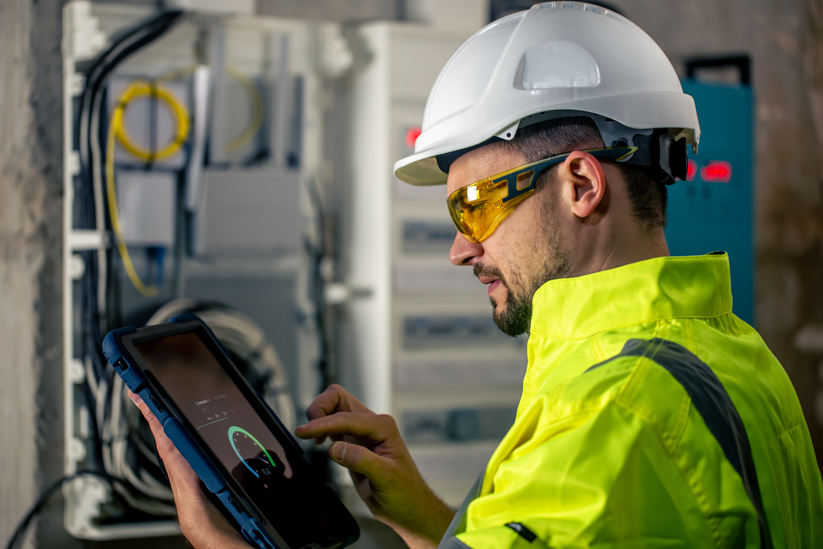 Man-an-Electrical-Technician-Working-in-a-Switchboard-With-Fuses-Uses-a-Tablet-Internet-in-Construction