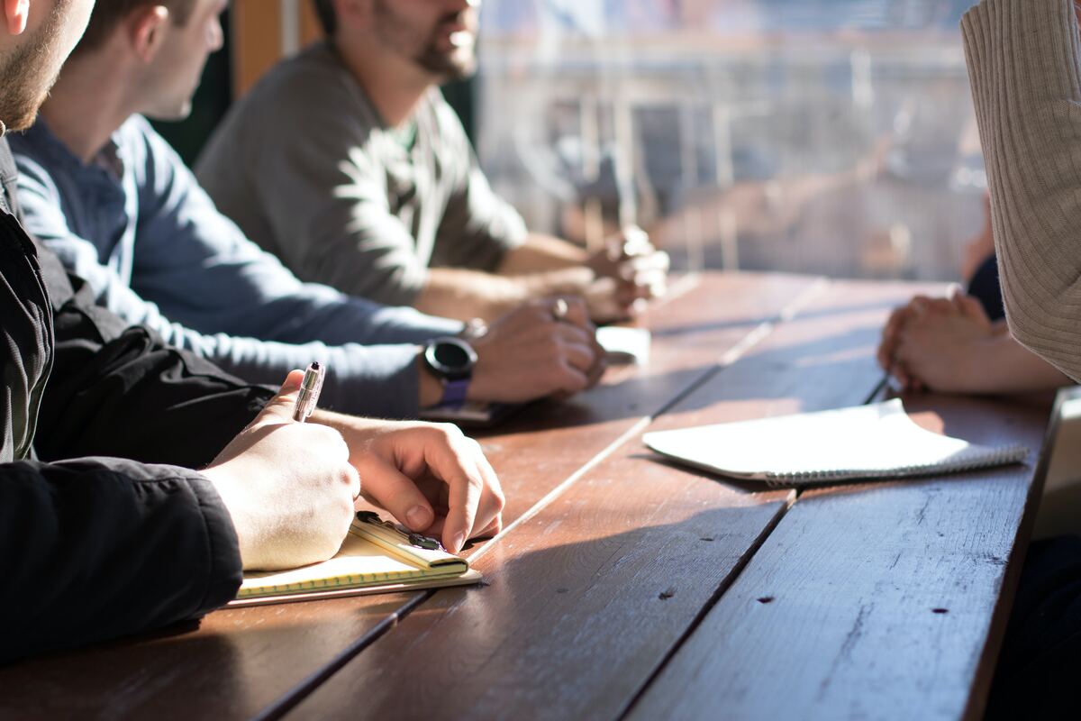 People-Sitting-On-Chair-In-Front-Of-Table-While-Holding-Pens-During-Daytime-Construction-Scheduling