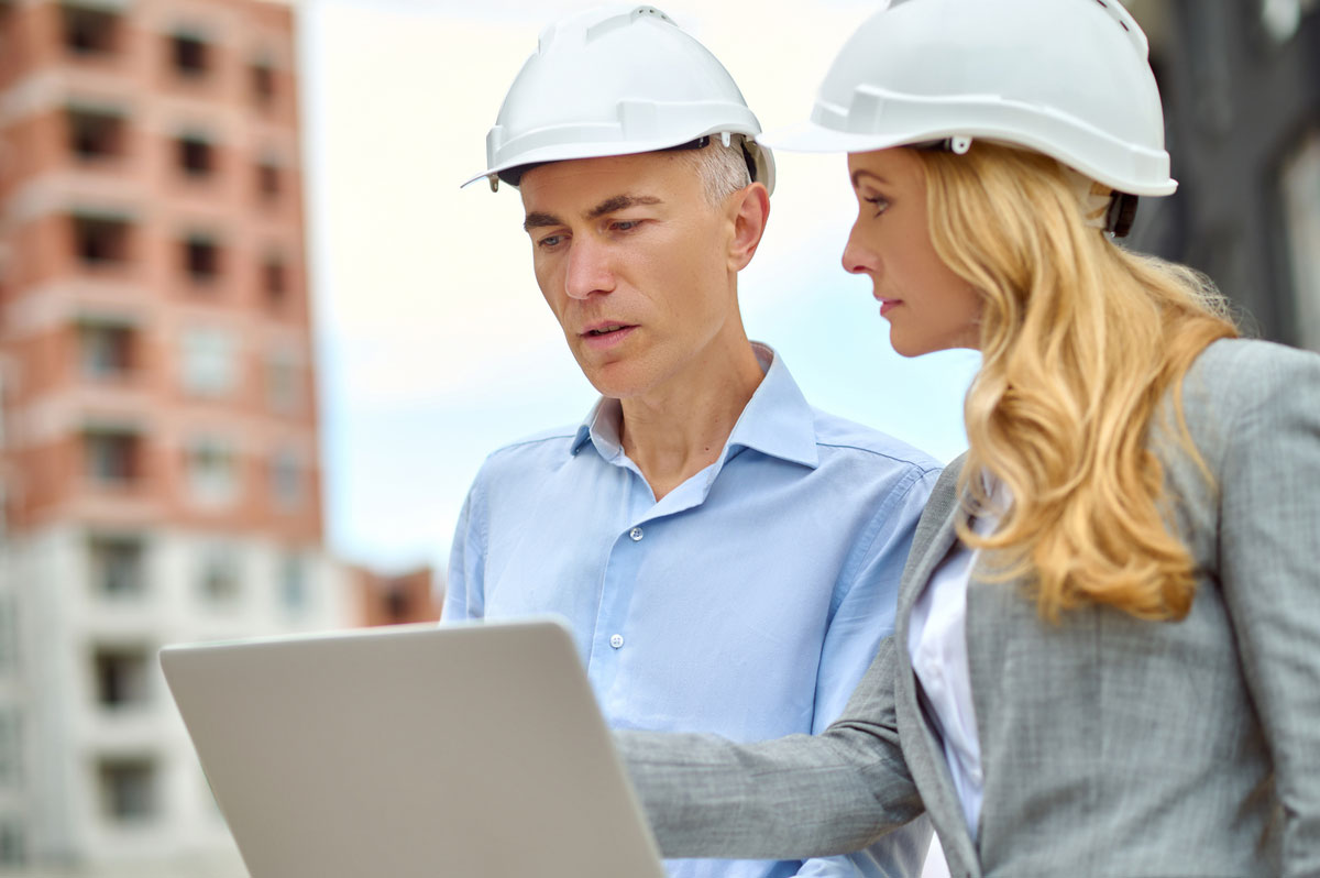 question-profile-demanding-business-woman-with-long-blond-hair-protective-helmet-looking-attentively-talking-man-with-laptop-standing-construction-site-IoT-Consulting-Services