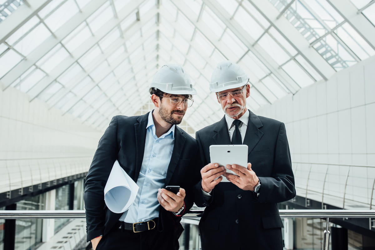 Two-Successful-Entrepreneur-Helmet-With-Project-Laptop-New-Buildings-Stay-Near-Glass-Roof-Construction-Insurance-Companies