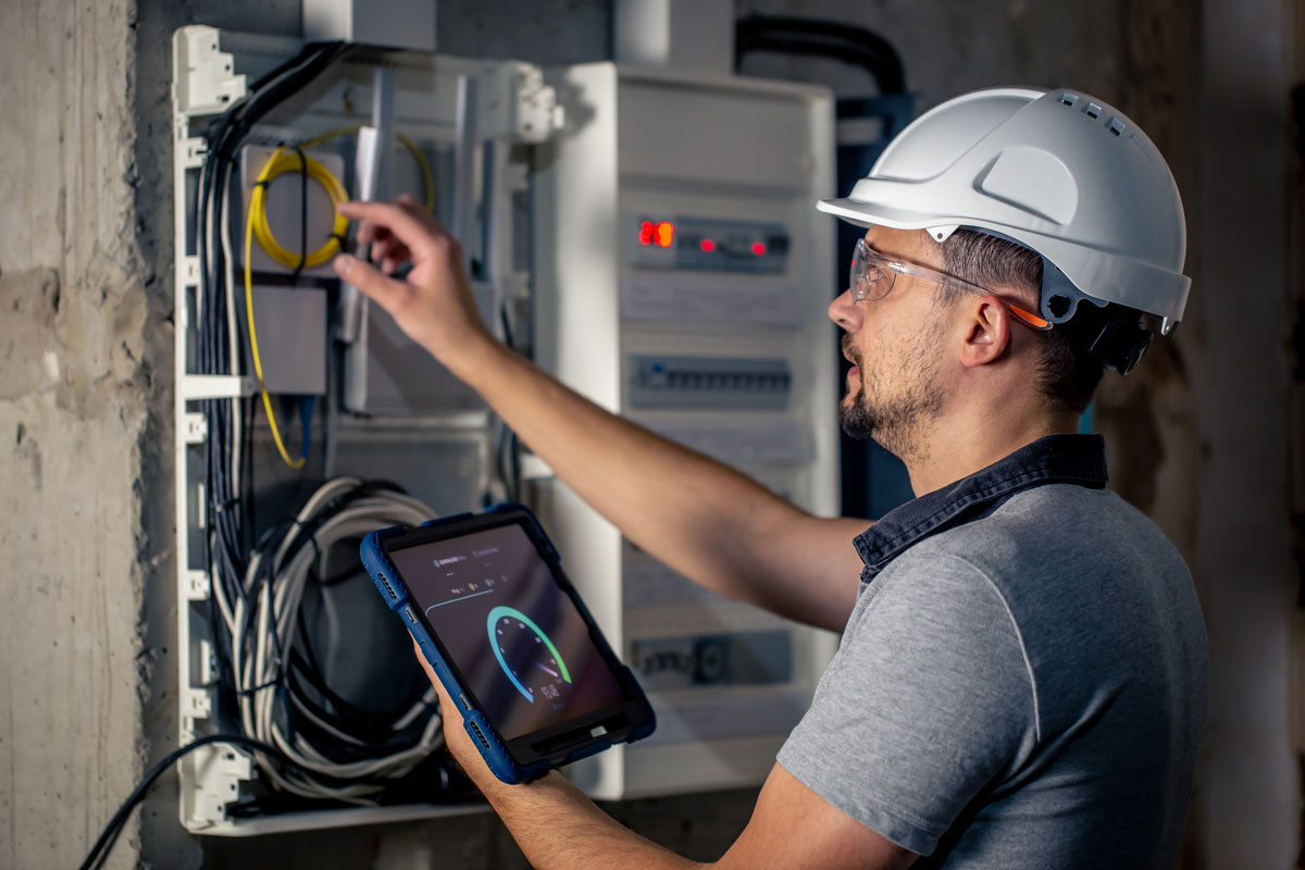 Man-Electrical-Technician-Working-Switchboard-With-Fuses-Uses-Tablet(2)-MEP-in-Construction