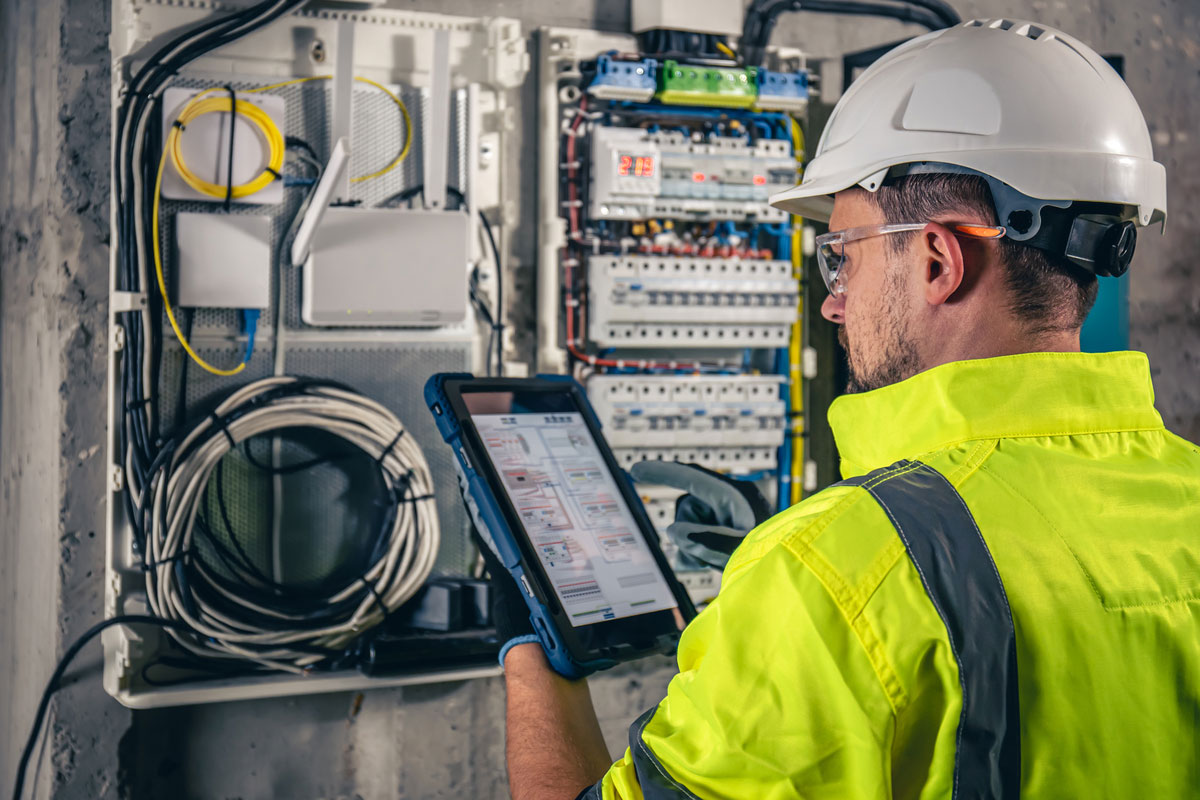 Man-Electrical-Technician-Working-Switchboard-With-Fuses-Uses-Tablet(1)-MEP-in-Construction