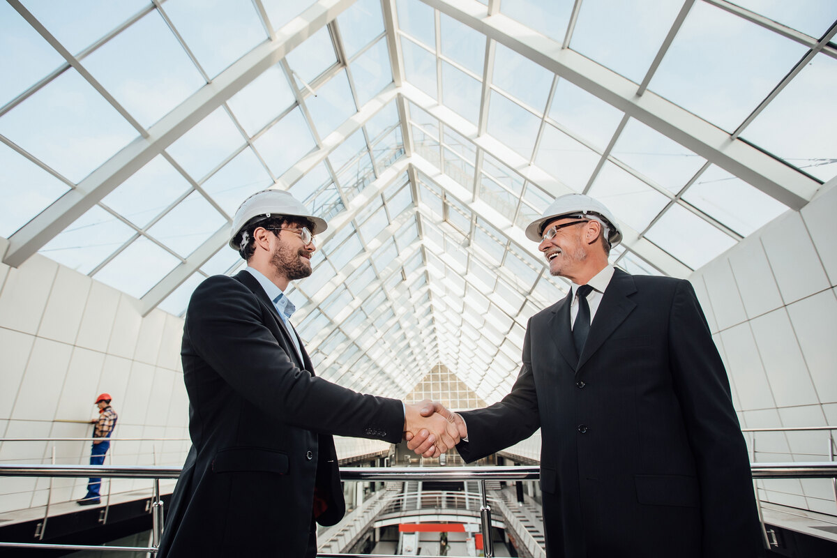 Two-cheerful-Businessman-Handshaking-Helmet-New-Building-Tender-in-Construction