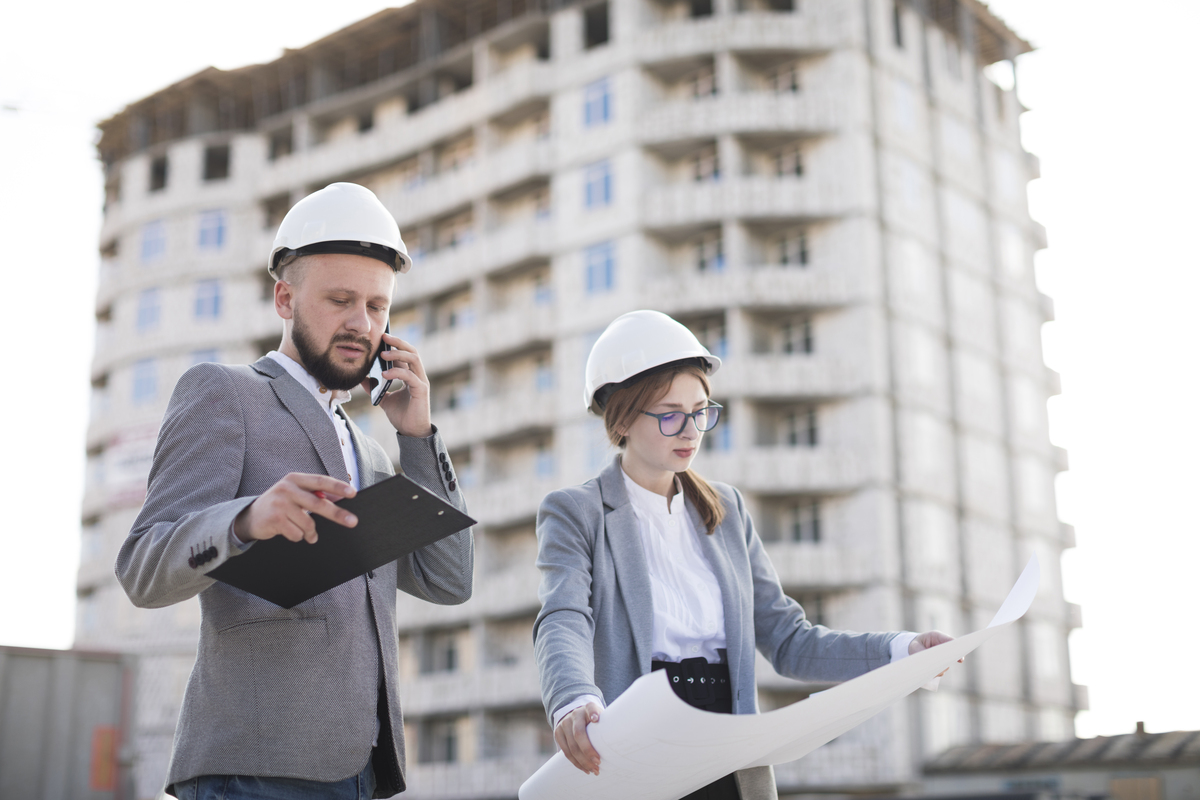 male-architecture-talking-cellphone-standing-near-female-architecture-holding-blueprint-construction-site-Construction-Company-in-Luxembourg